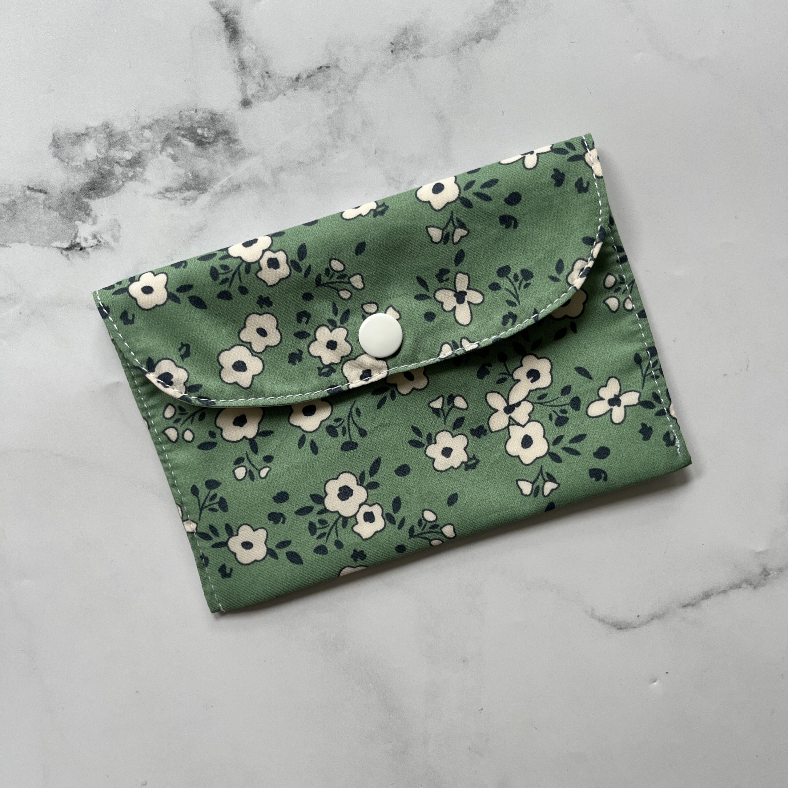 Pochette pour savon solide verte claire avec des fleurs écru et un feuillage bleu marine et un bouton pression pour fermer la pochette